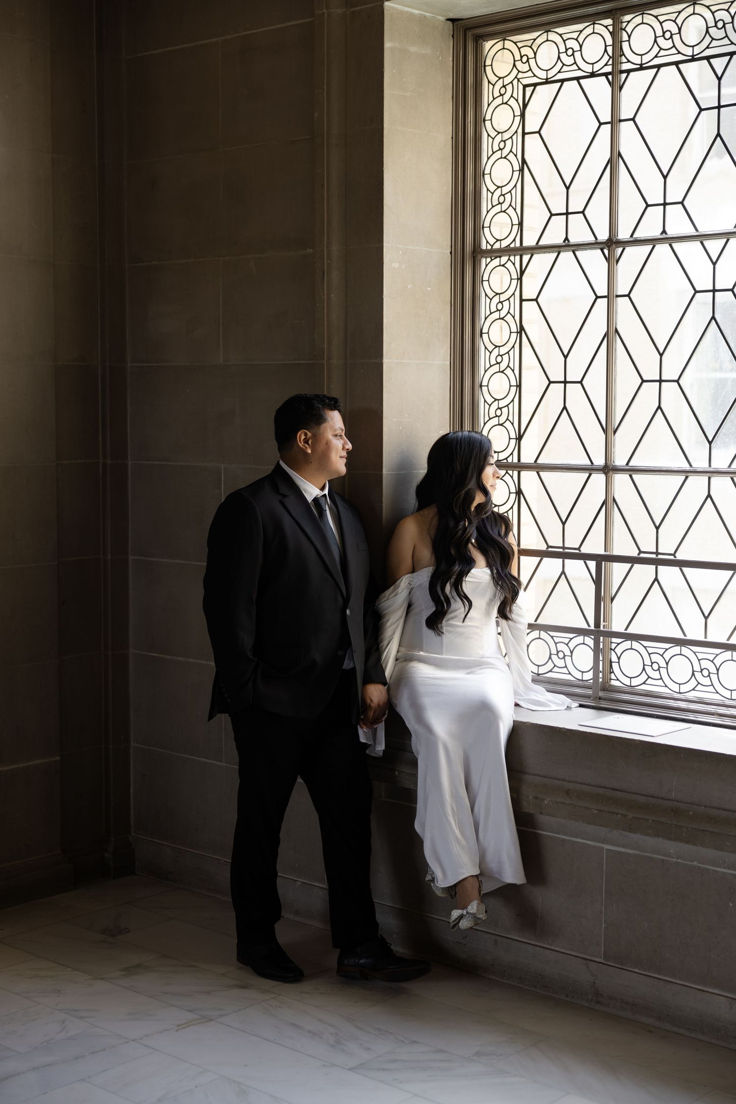 Couple standing by decorative windows in a minimalist interior with dramatic lighting.