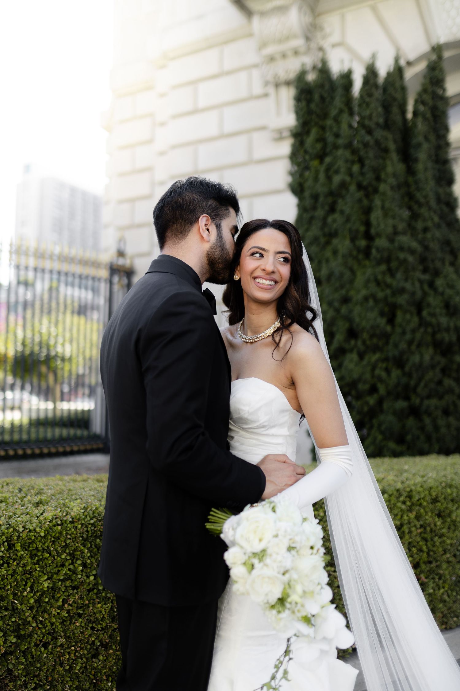 A bride and groom share intimate moments together in a garden setting with white flowers and greenery.