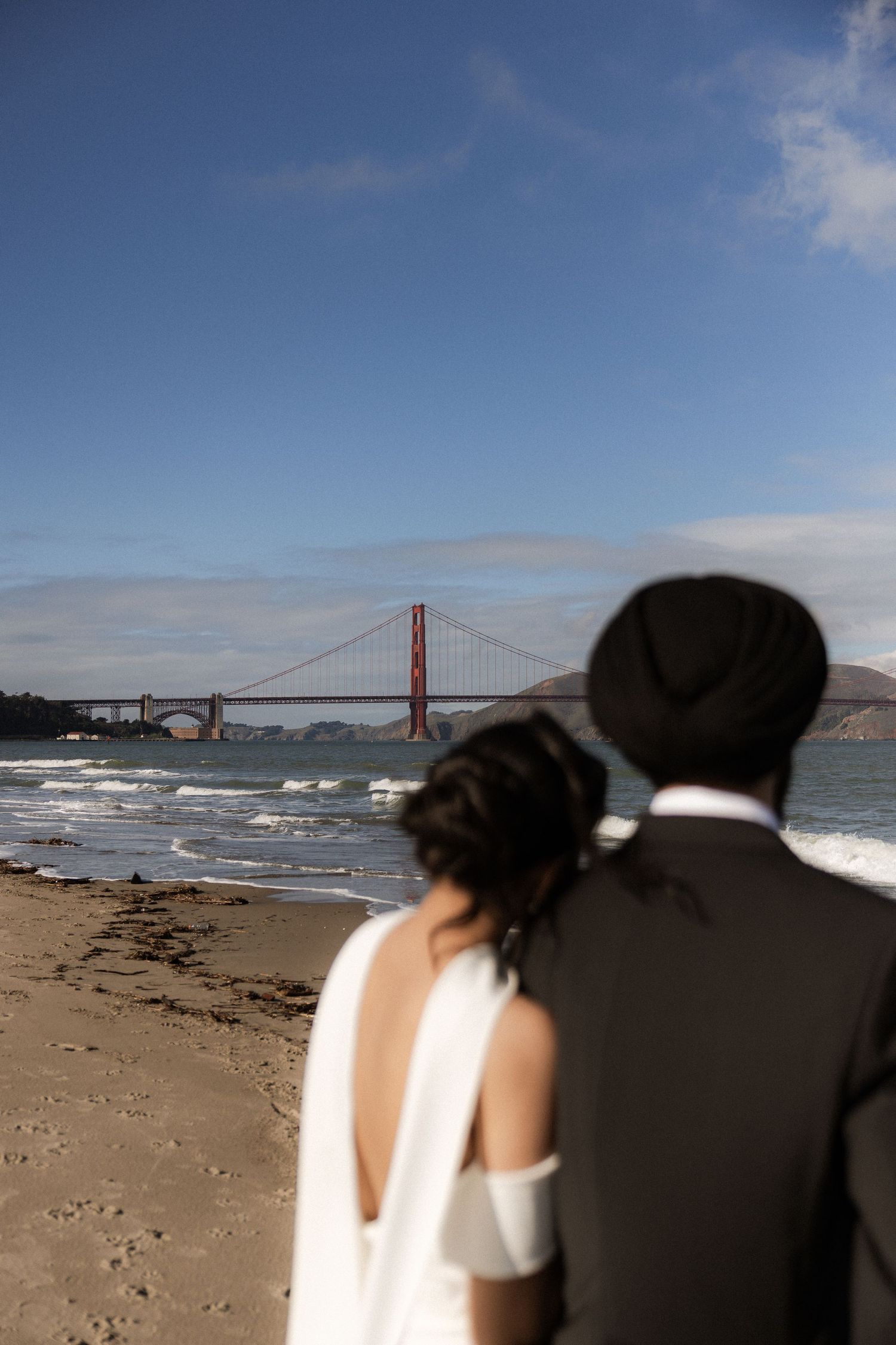 Couple admiring the Golden Gate Bridge from a sandy beach on a sunny day in San Francisco.