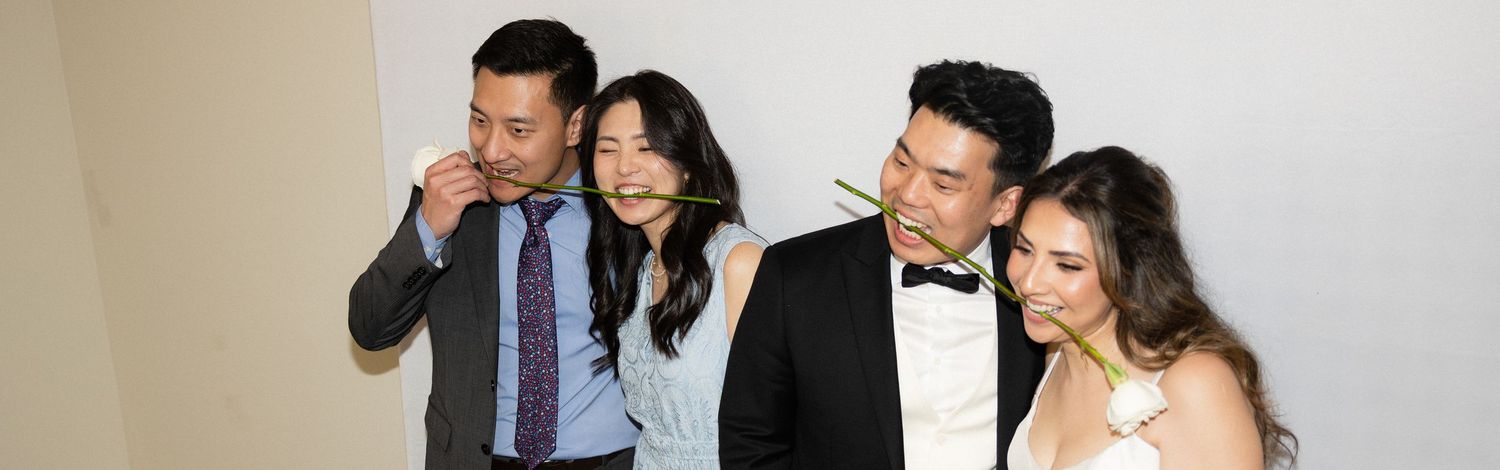 Two couples in formal wedding attire pose together for a fun photo booth picture at a reception.