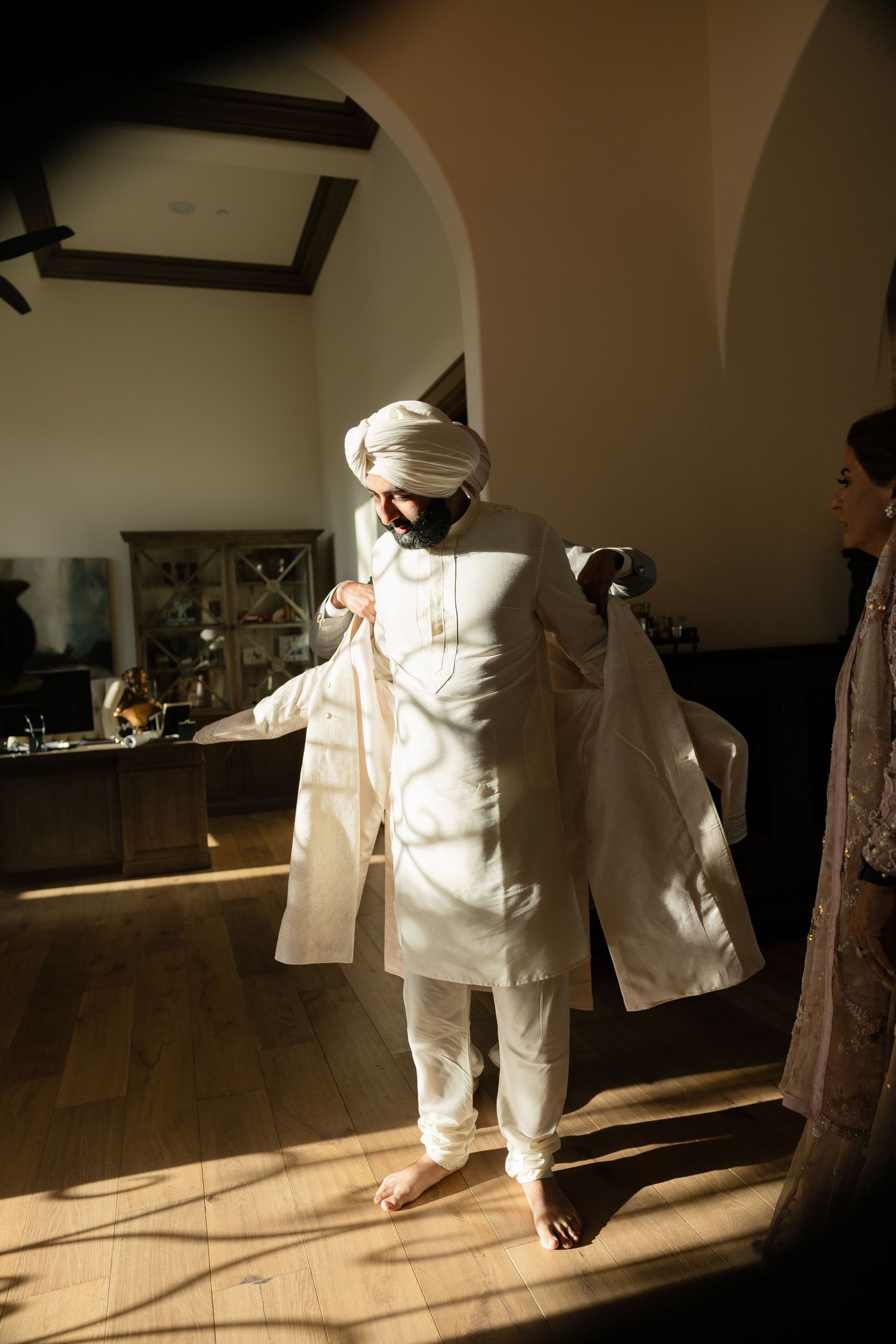Sunlight streams through windows onto a figure in white traditional attire performing graceful movements in an indoor space.