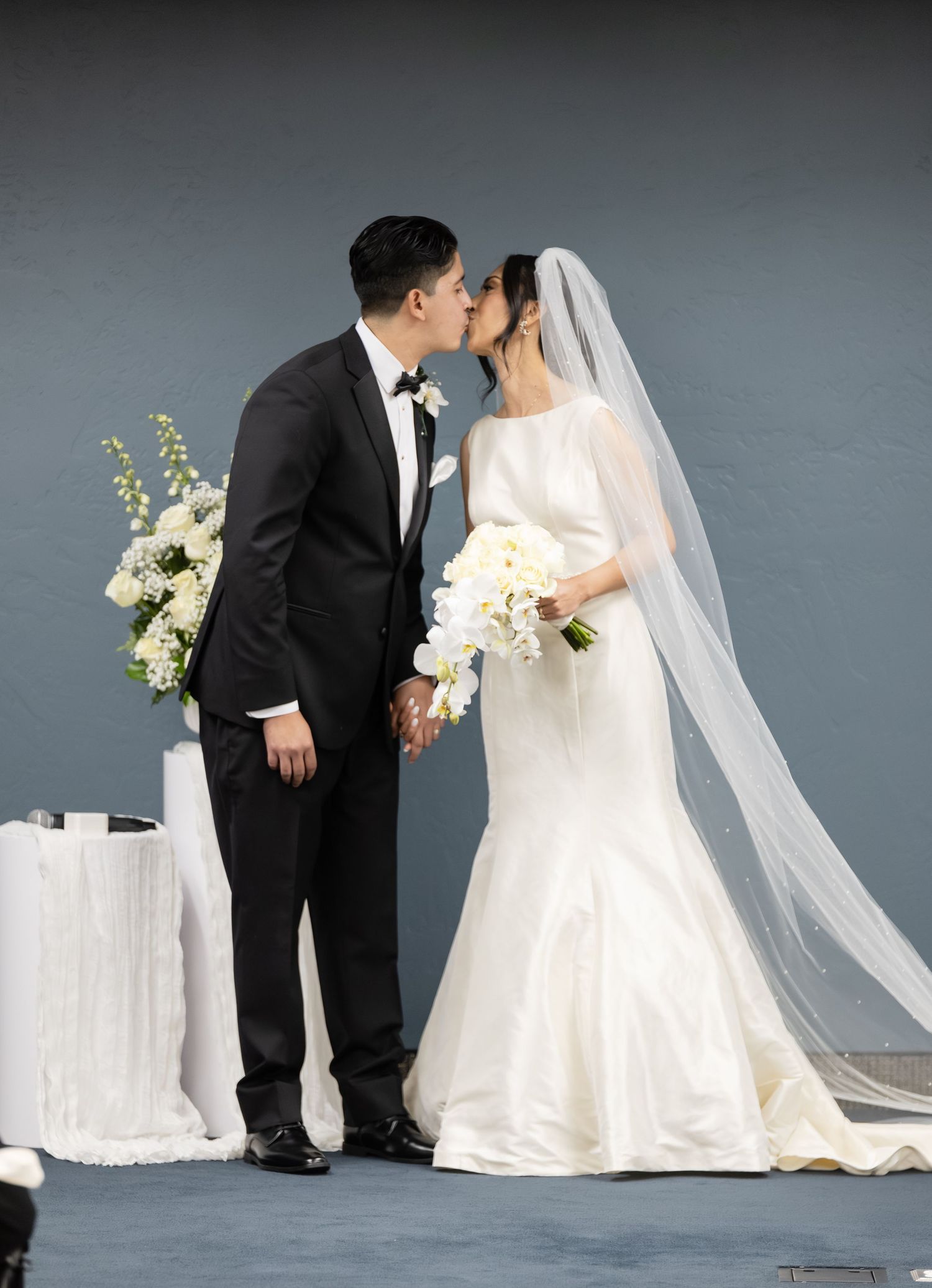Wedding portrait with elegant white floral arrangements and flowing bridal veil.