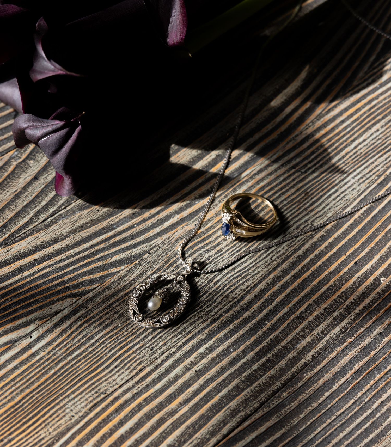 Wedding rings and flowers creating dramatic shadows on wooden surface.