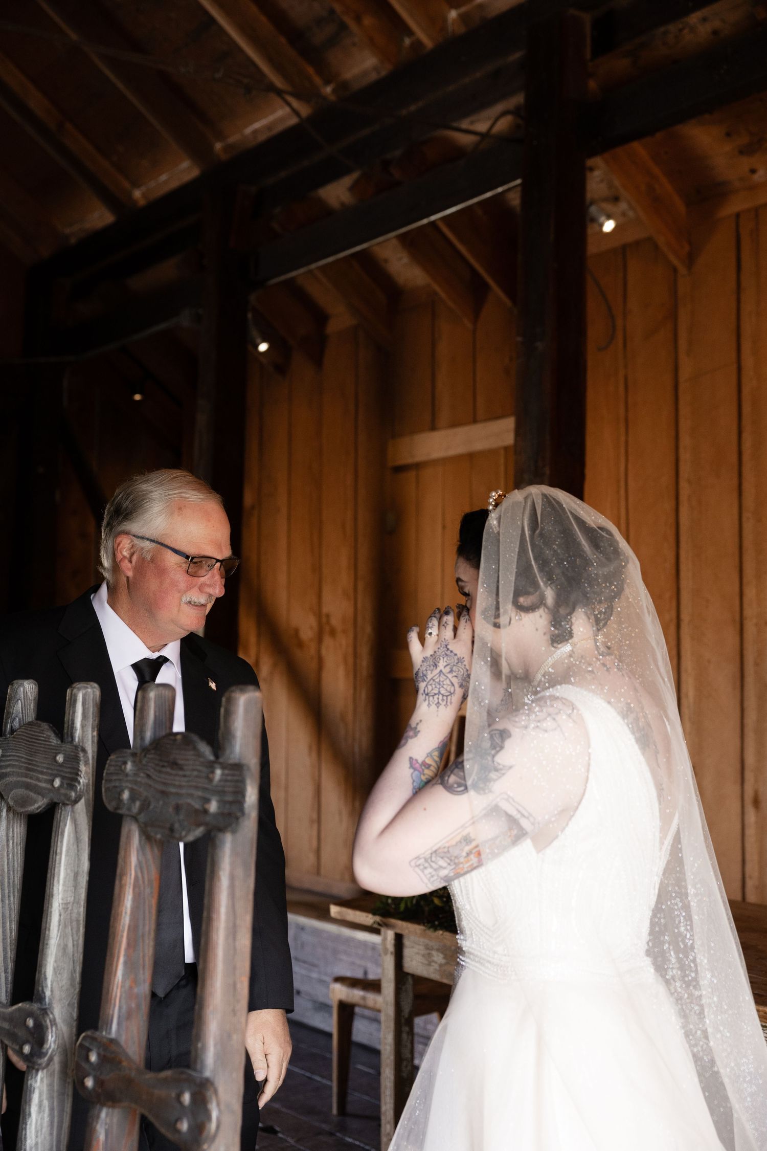 A tender embrace between two people in formal attire inside a rustic wooden barn setting.