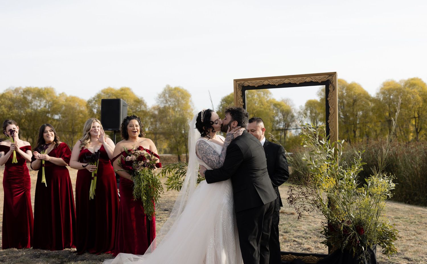 Scenic outdoor wedding setup with burgundy bridesmaids and wooden arch against desert backdrop.