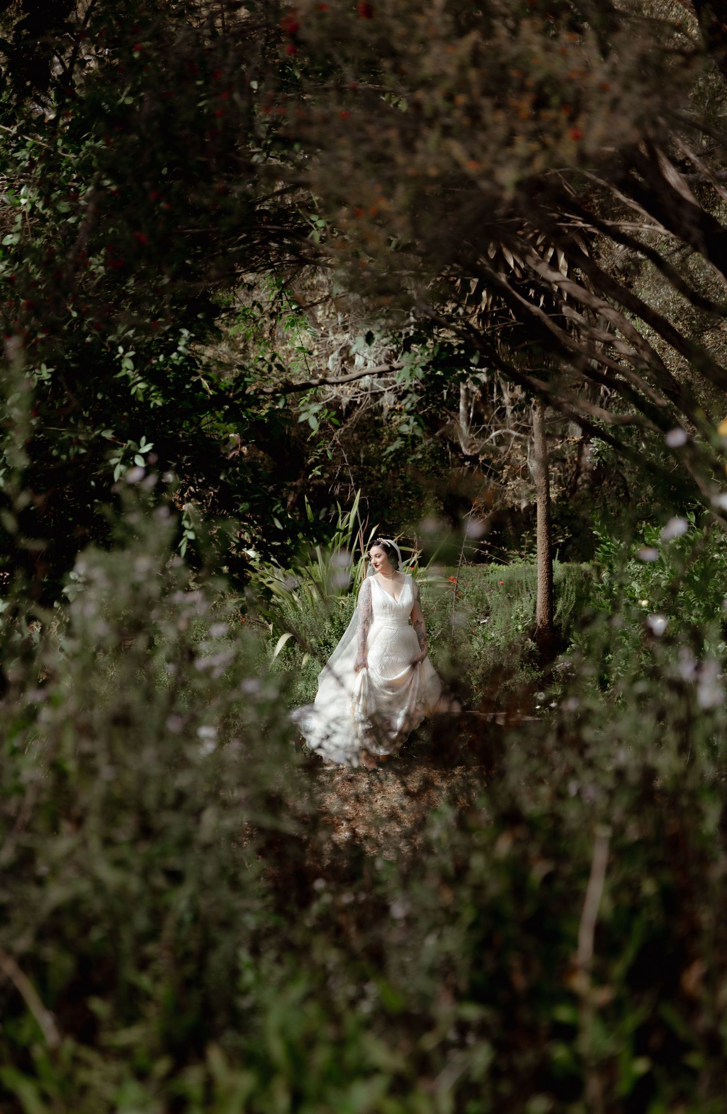 Bride in white dress framed by lush garden greenery and natural lighting.