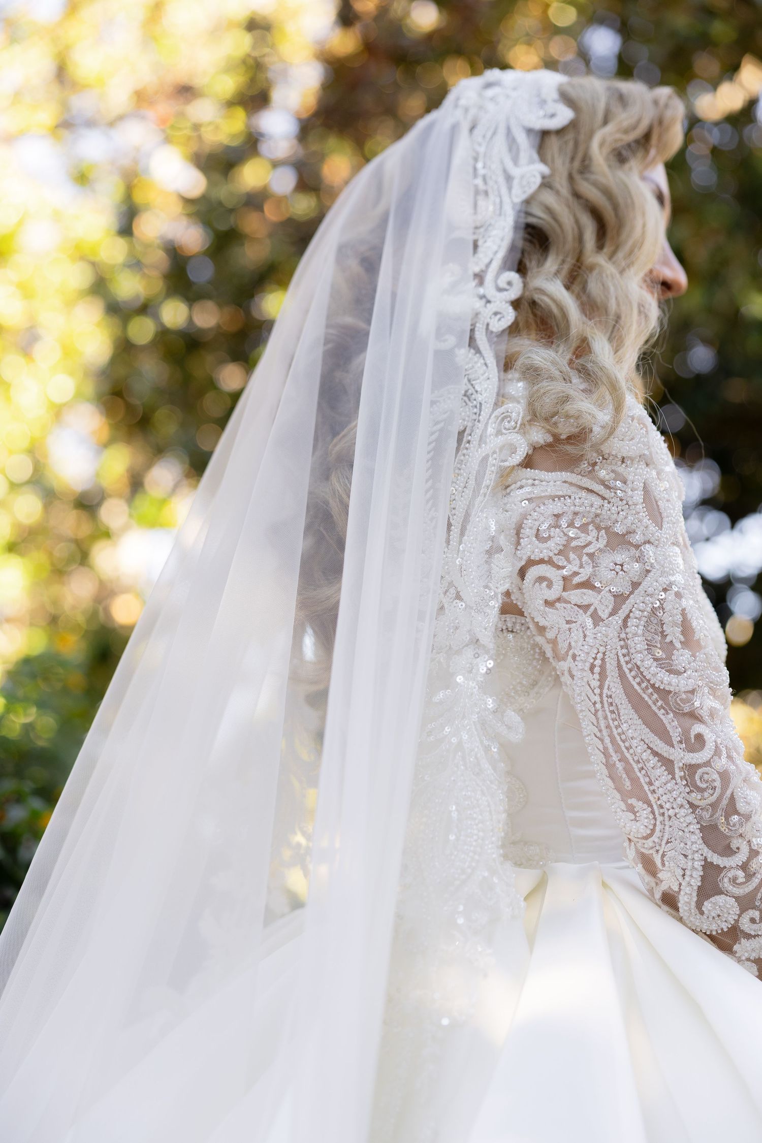 Side view of intricate lace detailing on wedding dress with flowing veil.