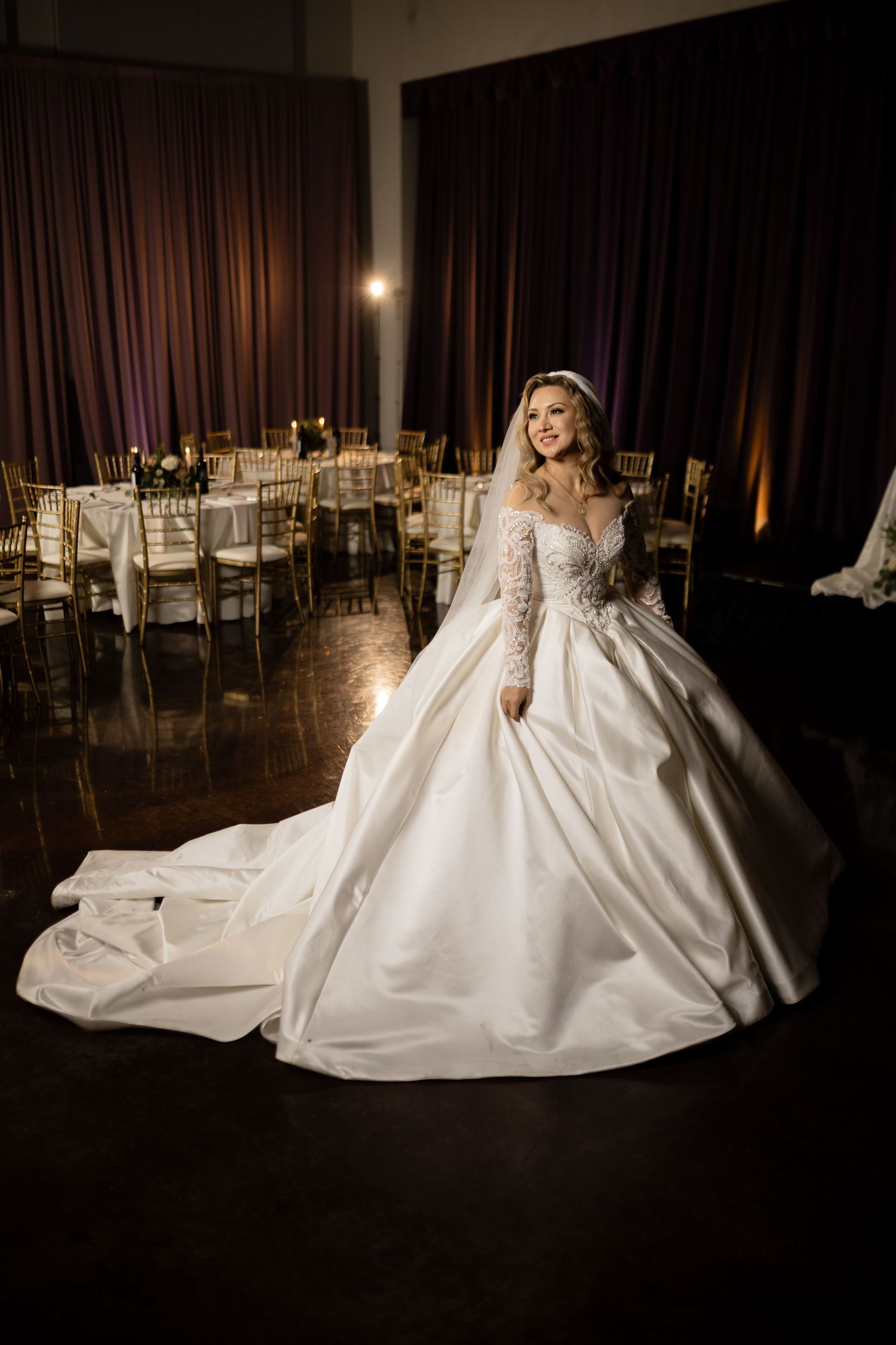 A dramatic bridal portrait in a reception venue with gold chairs and dark curtains.