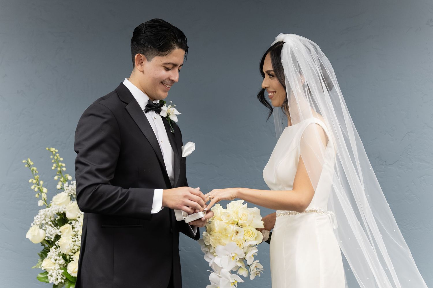 Intimate wedding portrait moment with couple sharing smiles against grey backdrop.