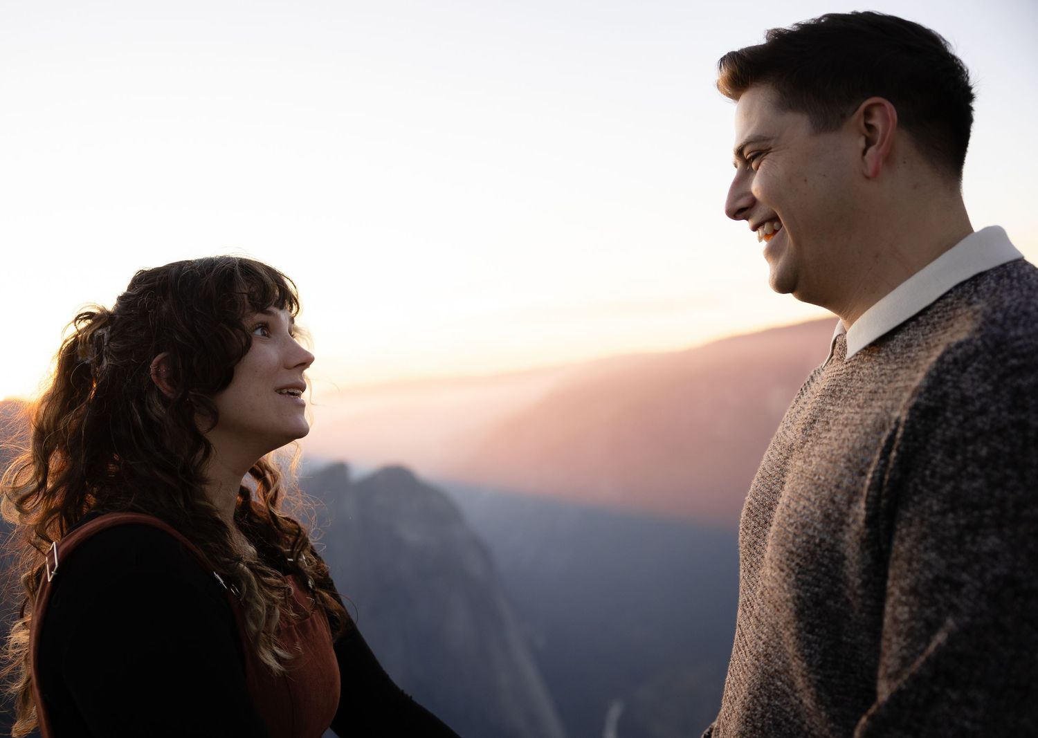A romantic couple embraces while watching sunset over mountain peaks at Yosemite.