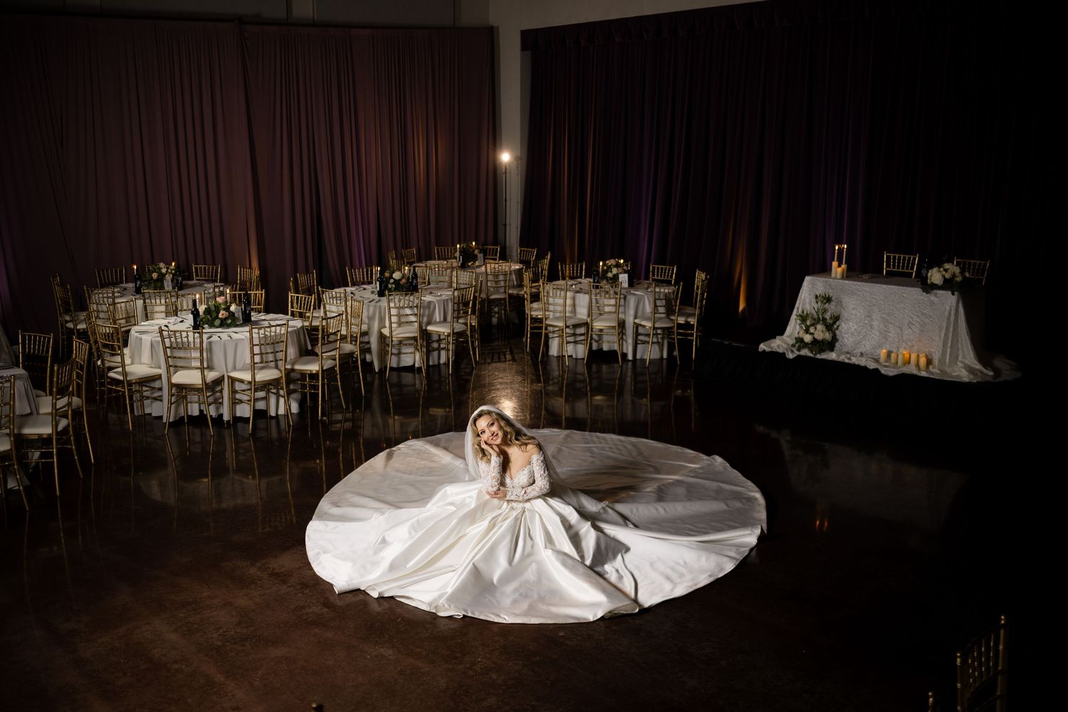 An artistic overhead shot of a white wedding gown spread out on a dark ballroom floor.