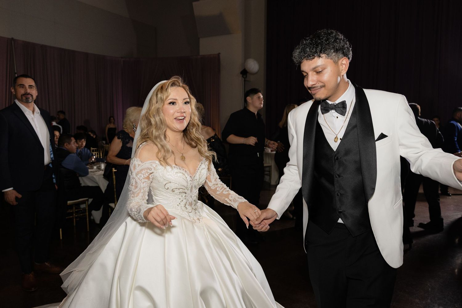 Couple dances together at wedding reception with bride in ballgown and groom in white tuxedo jacket.