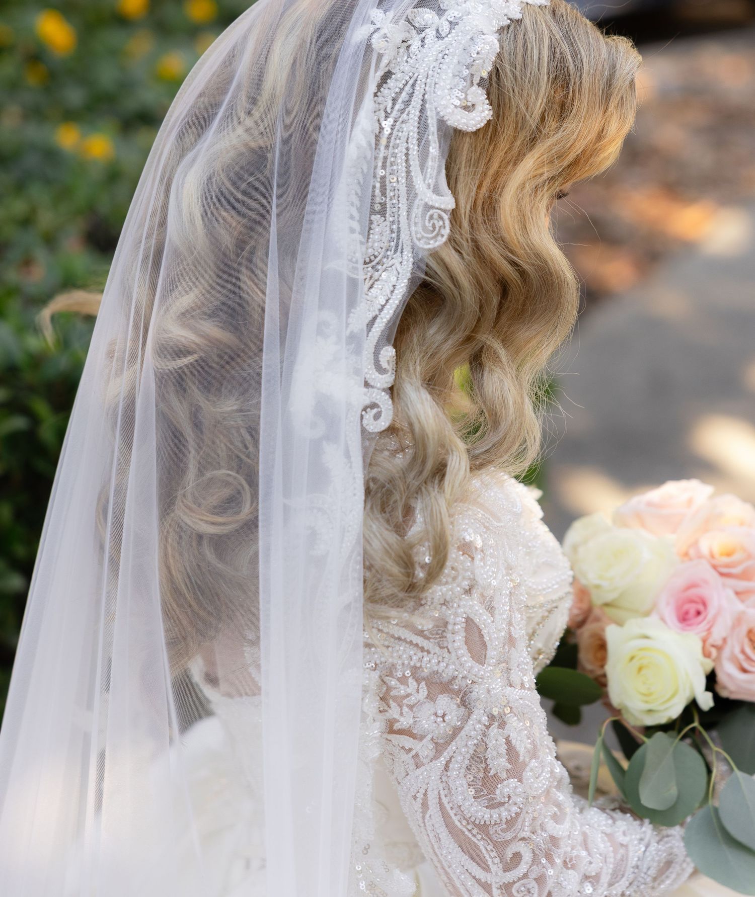 Detailed back view of lace wedding dress with flowing veil in garden setting.