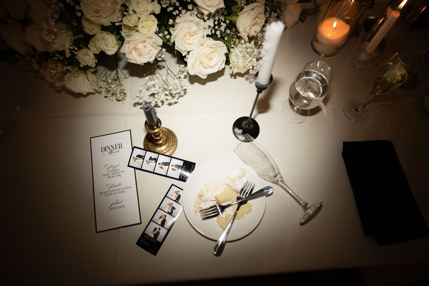 Wedding reception table with dinner menu, photo strips, champagne flutes and white roses.