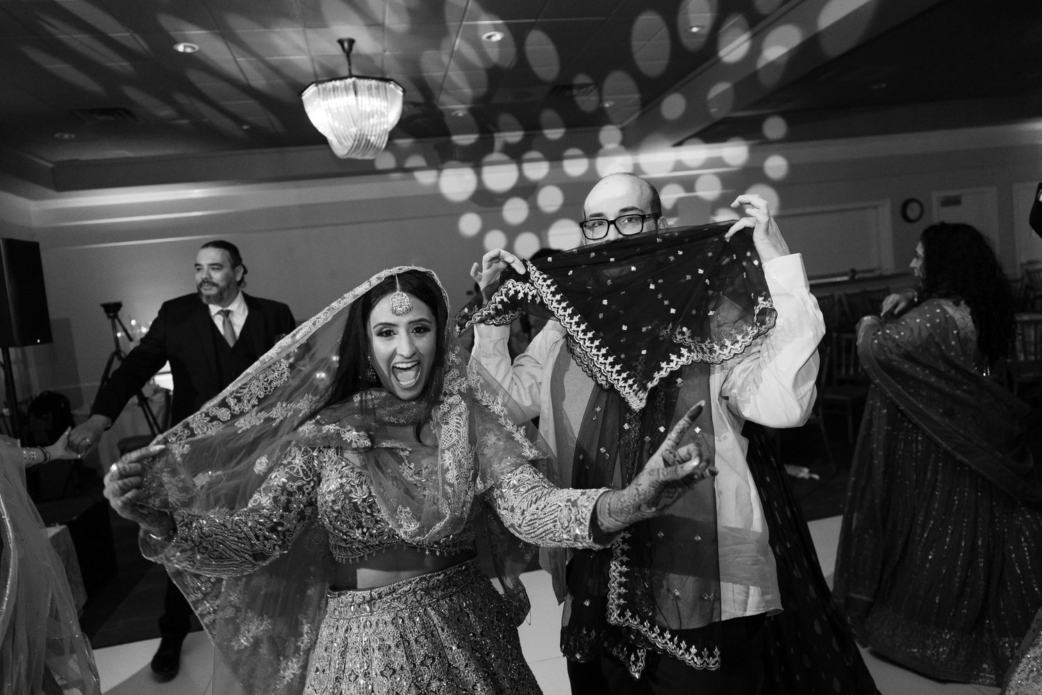 Wedding guests dancing and celebrating on a dimly lit dance floor at an elegant reception venue.