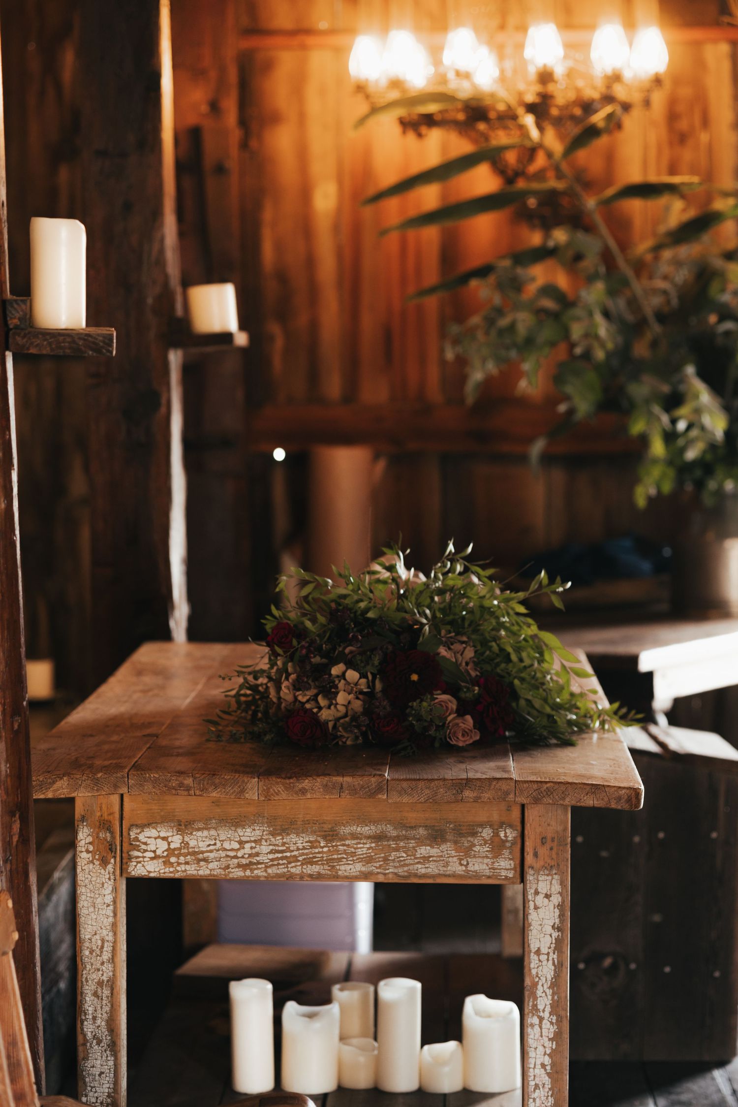 Rustic wooden table decorated with candles and greenery in barn setting.