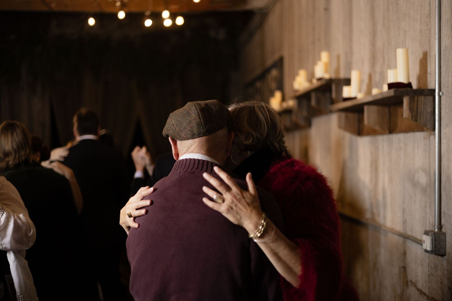 Wedding guests dancing together in dimly lit rustic reception space.