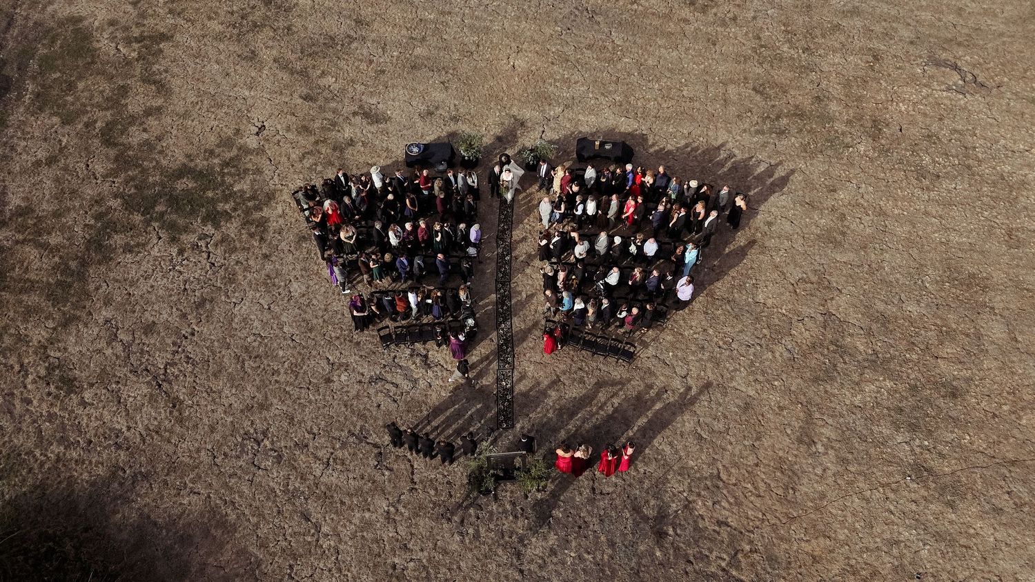 Aerial view of a large group of people arranged in a heart shape formation on brown terrain.