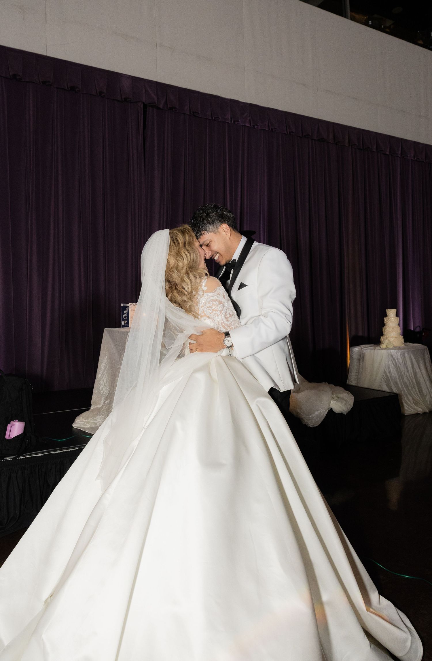 Romantic wedding couple shares intimate dance moment under dramatic lighting with flowing white ballgown.