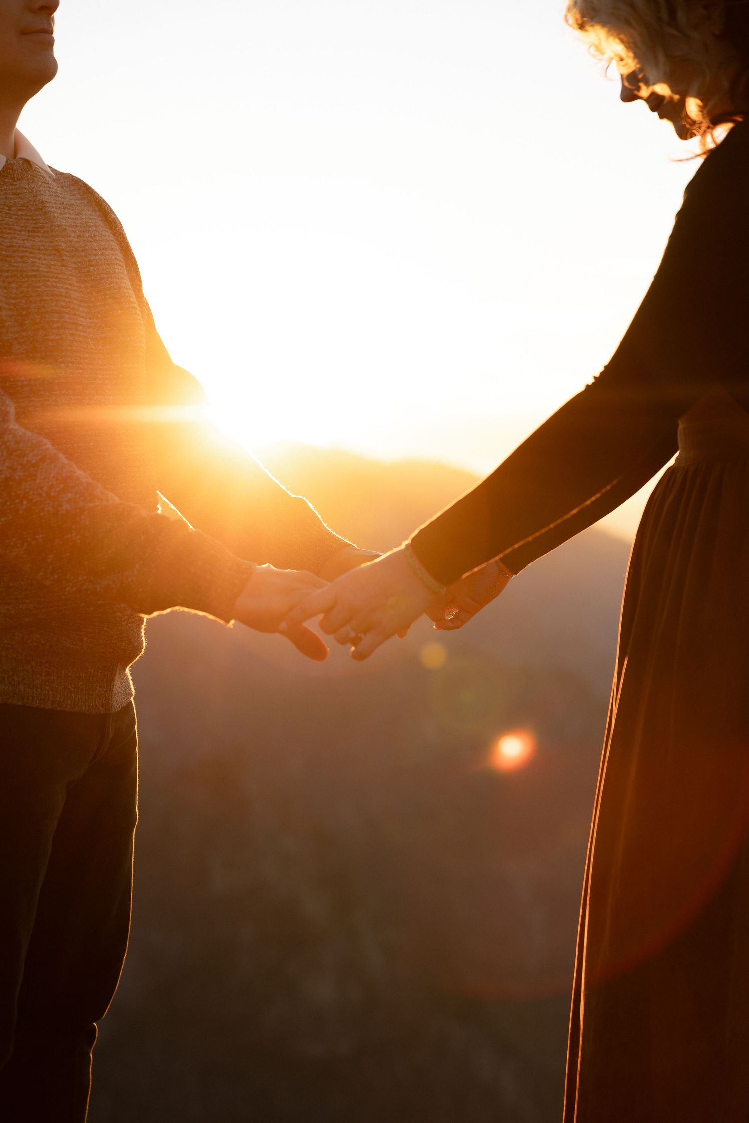 Hands reach out to connect in silhouette against a glowing sunset sky.