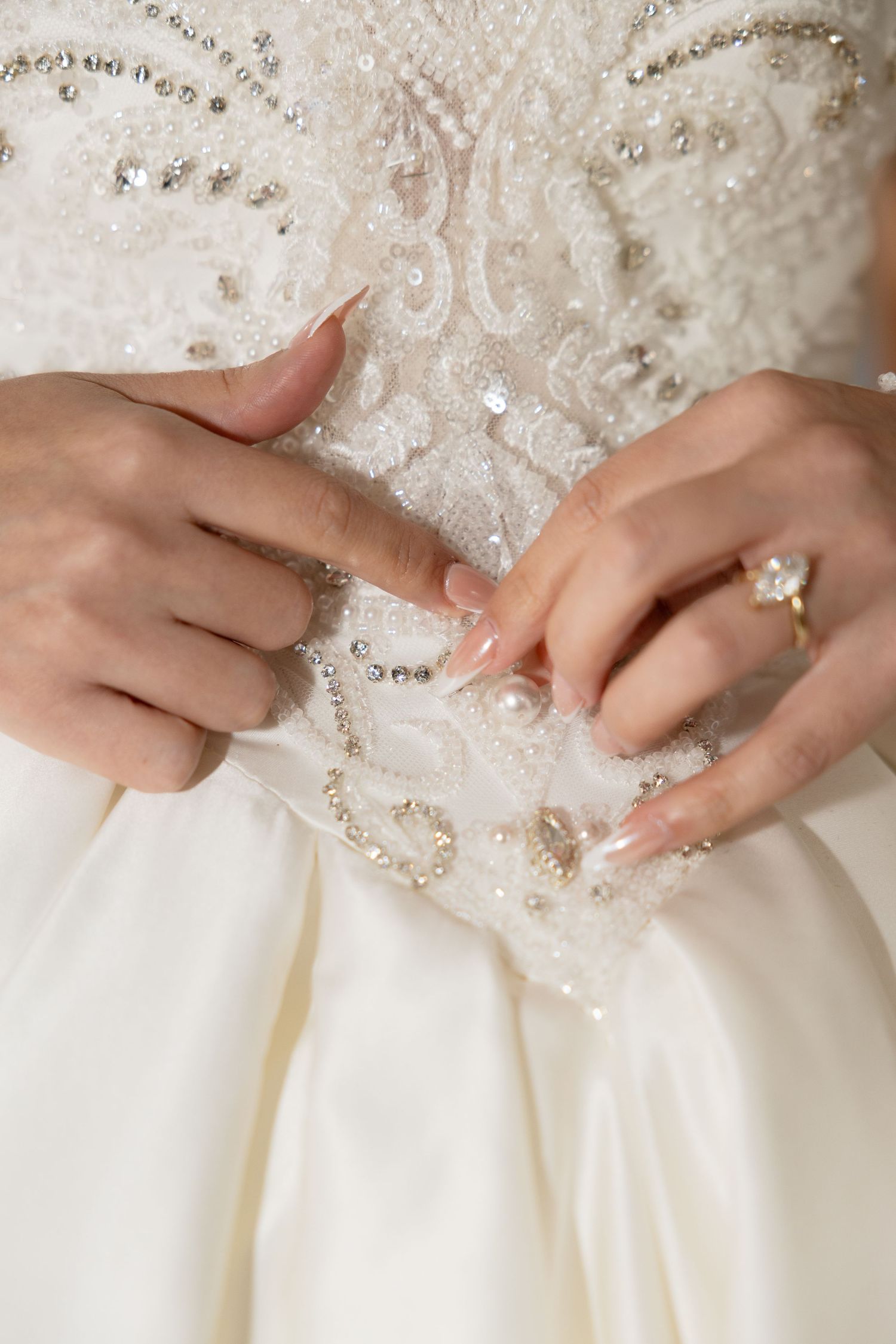 Delicate beading detail on an ivory wedding gown with hands adjusting the fabric.