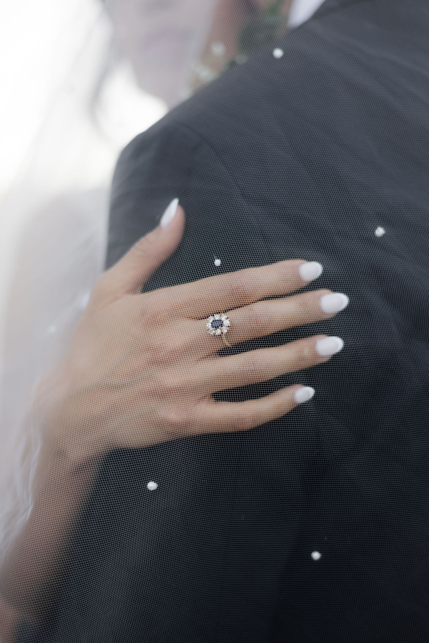 Close-up of an elegant engagement ring on a manicured hand against formal attire.