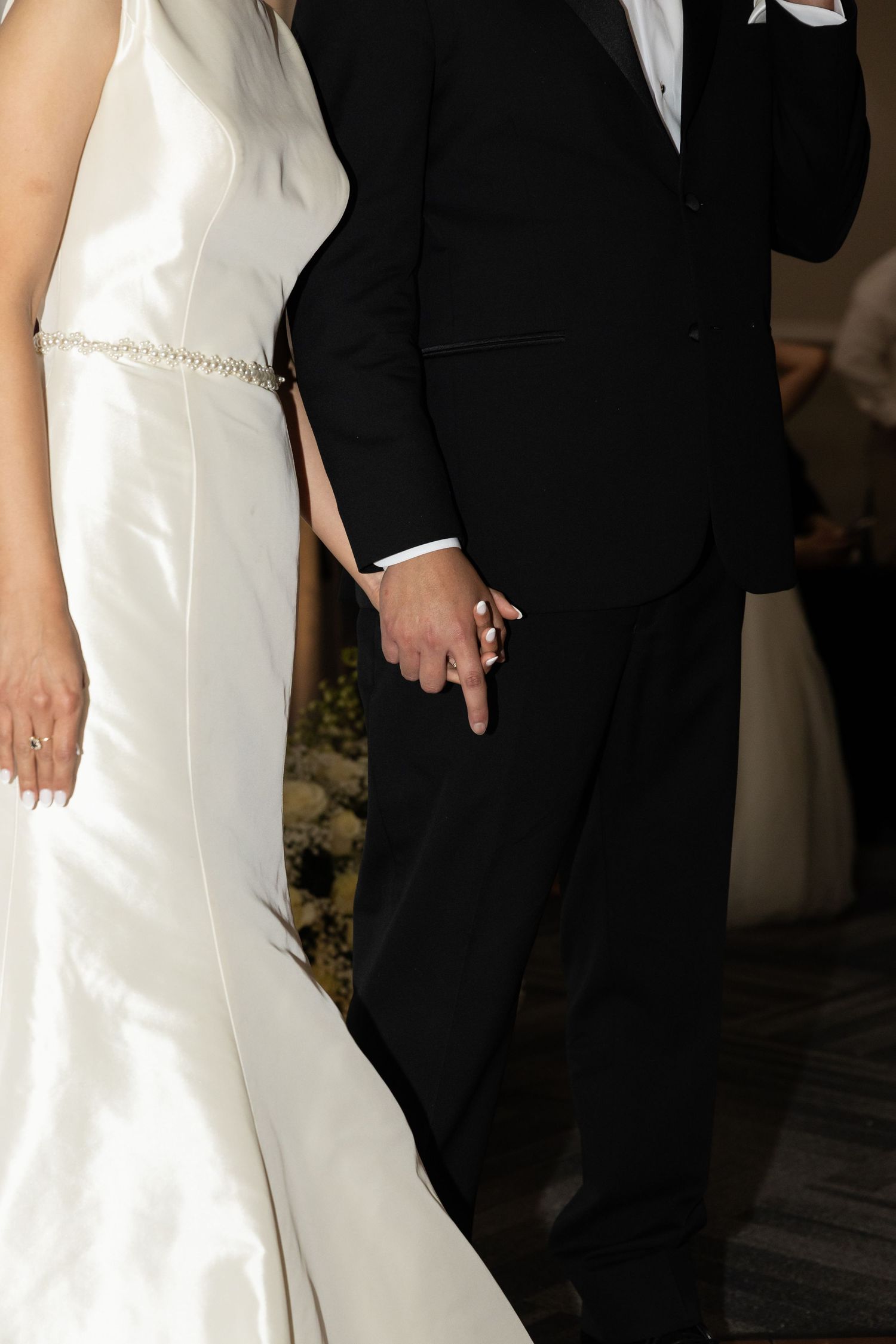 Close-up of bride and groom's formal attire showing white dress and black tuxedo details.