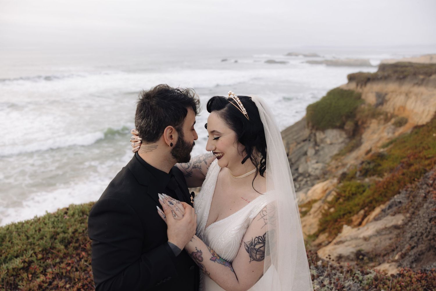 Romantic coastal wedding portrait with dramatic cliffs and ocean waves in background.