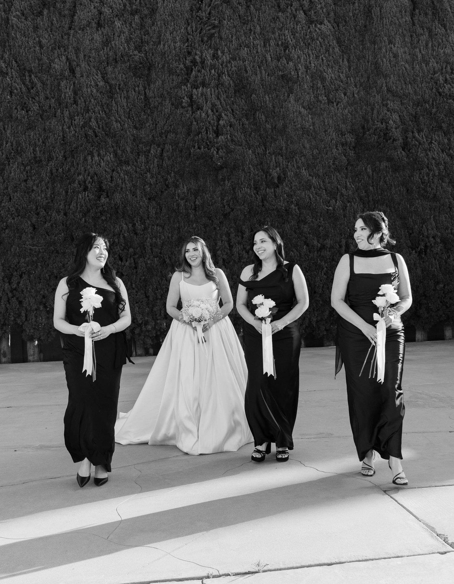 Black and white photo of a bride in a white gown with three bridesmaids in black dresses holding bouquets.