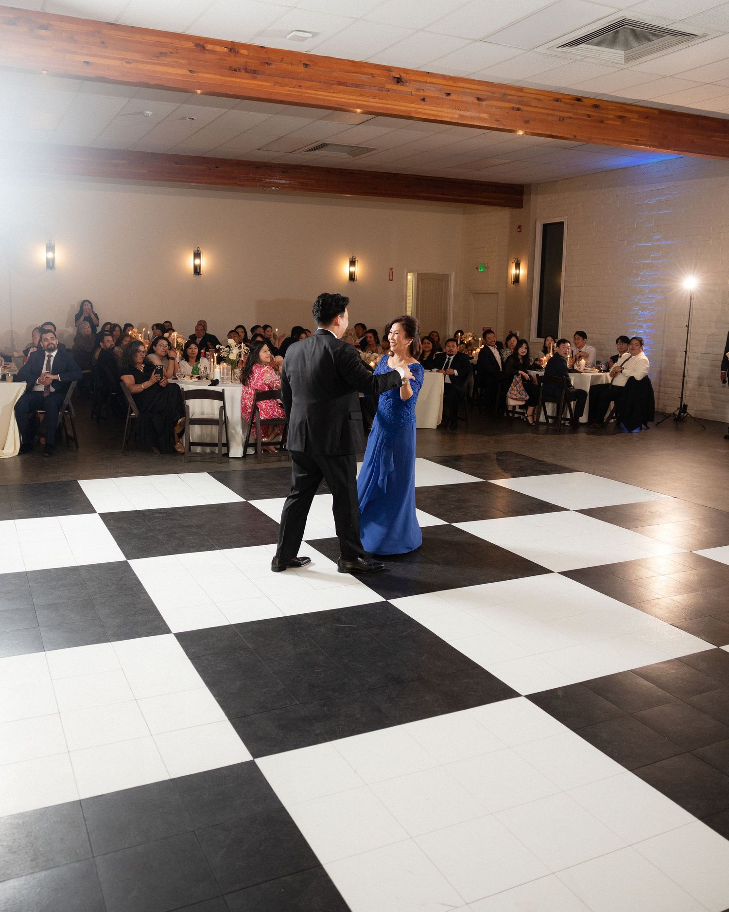 Couple shares elegant first dance on black and white checkered floor at wedding reception.