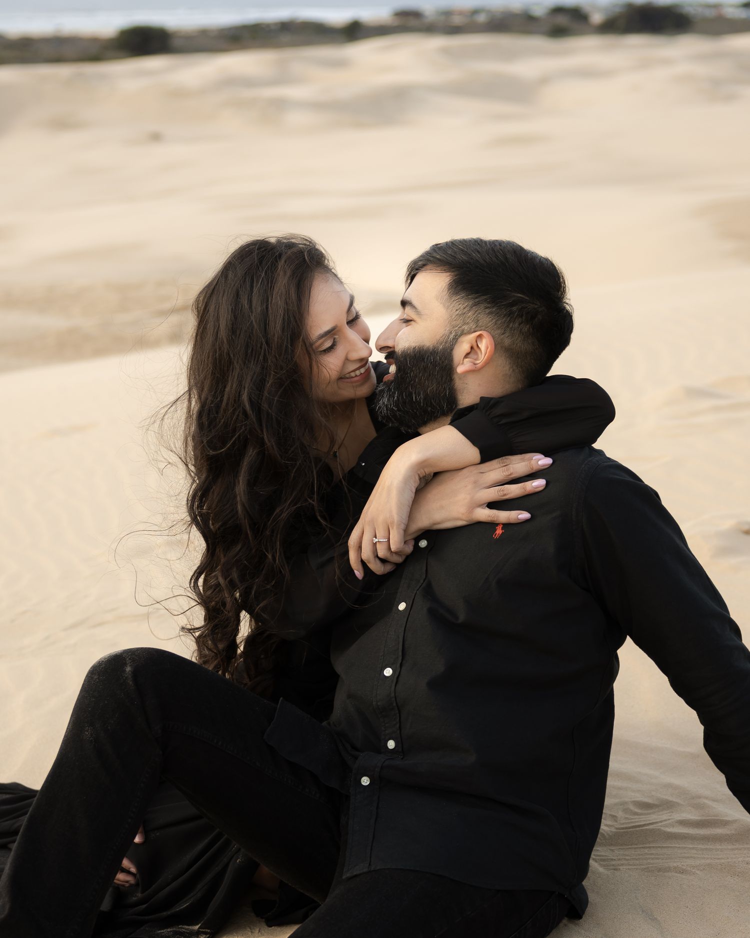 A romantic couple embraces and kisses on a sandy beach during a moody overcast day.
