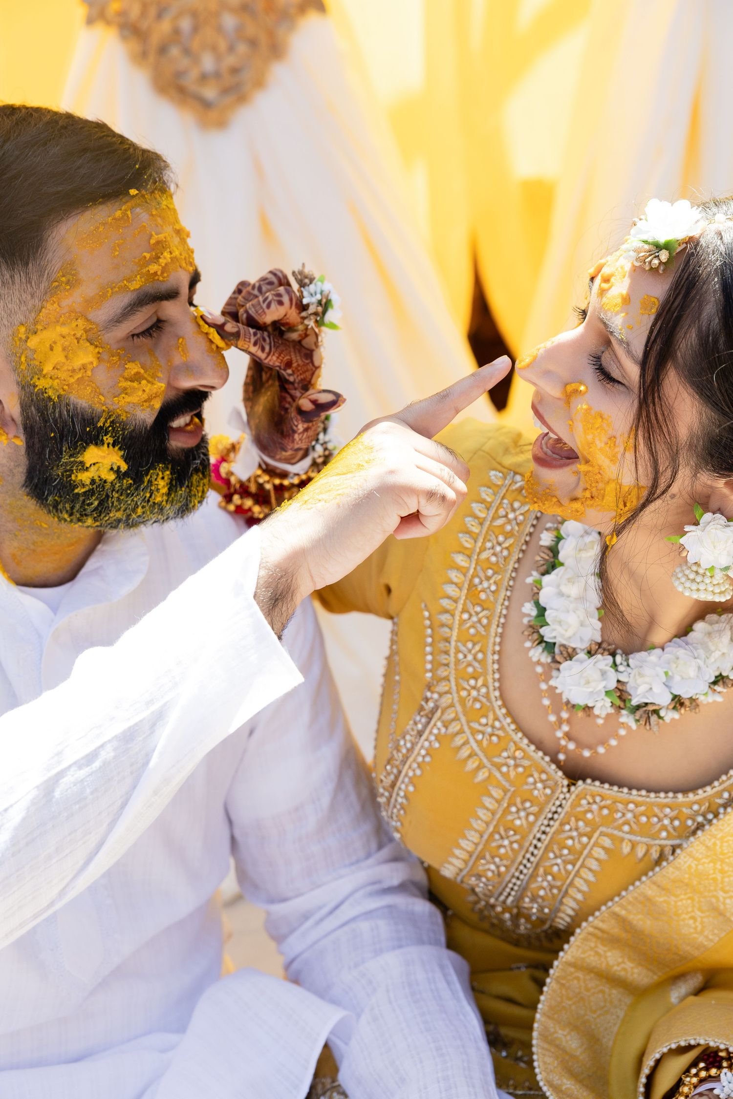 A couple in traditional wedding attire sharing an intimate moment against a warm yellow backdrop.