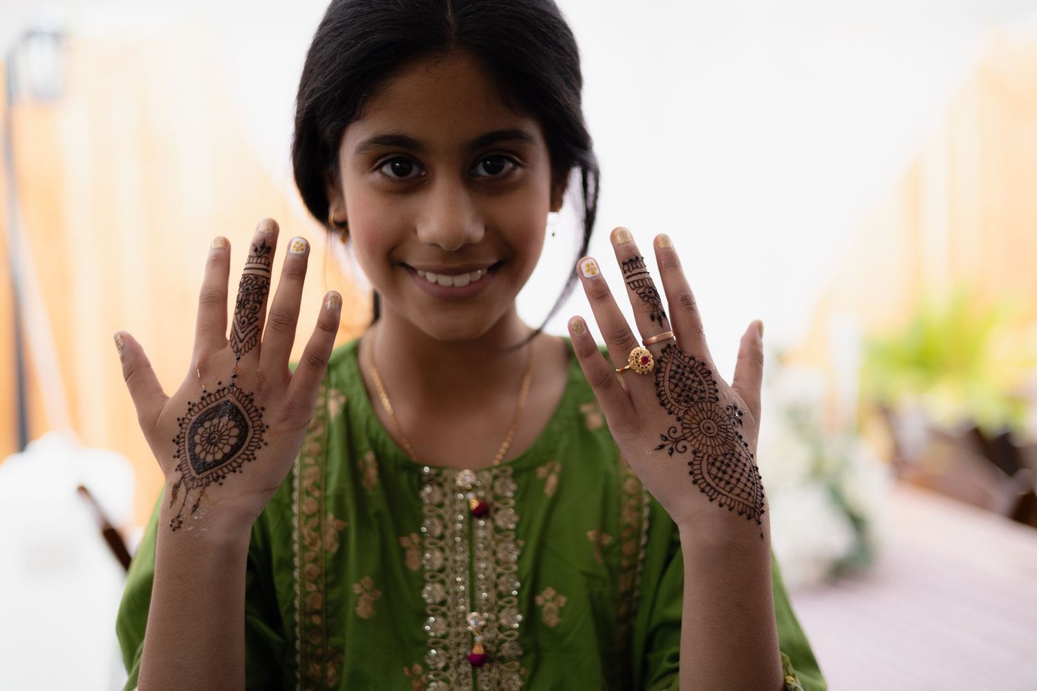 Beautiful intricate henna designs displayed on both palms while wearing a traditional green embroidered outfit.