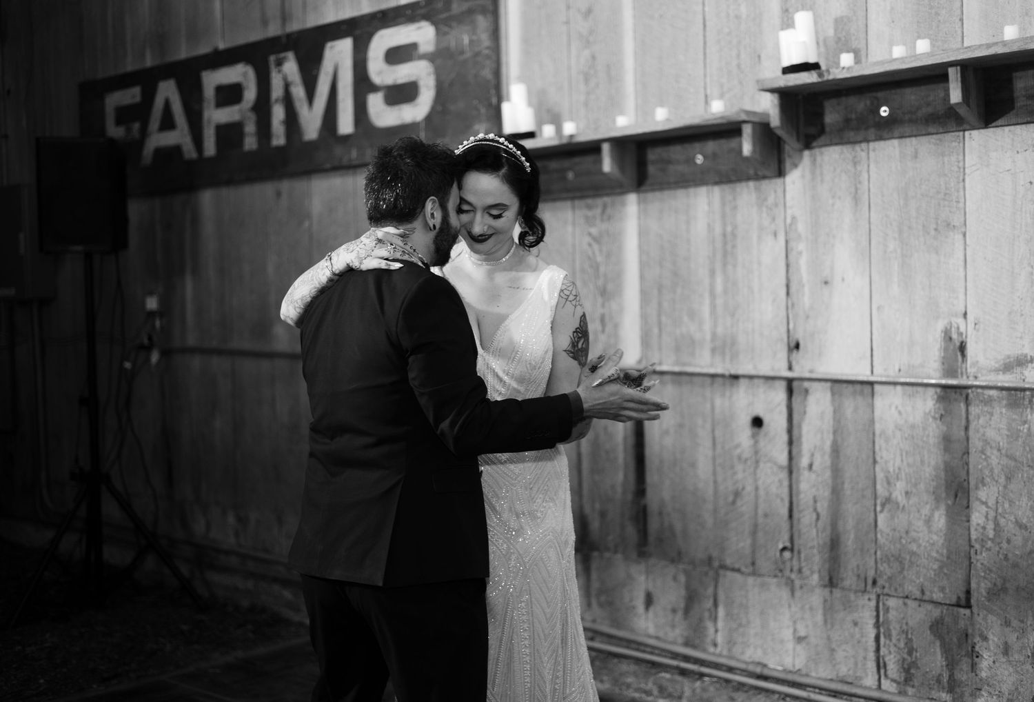 Black and white photo of a couple dancing in a rustic barn venue with string lights.
