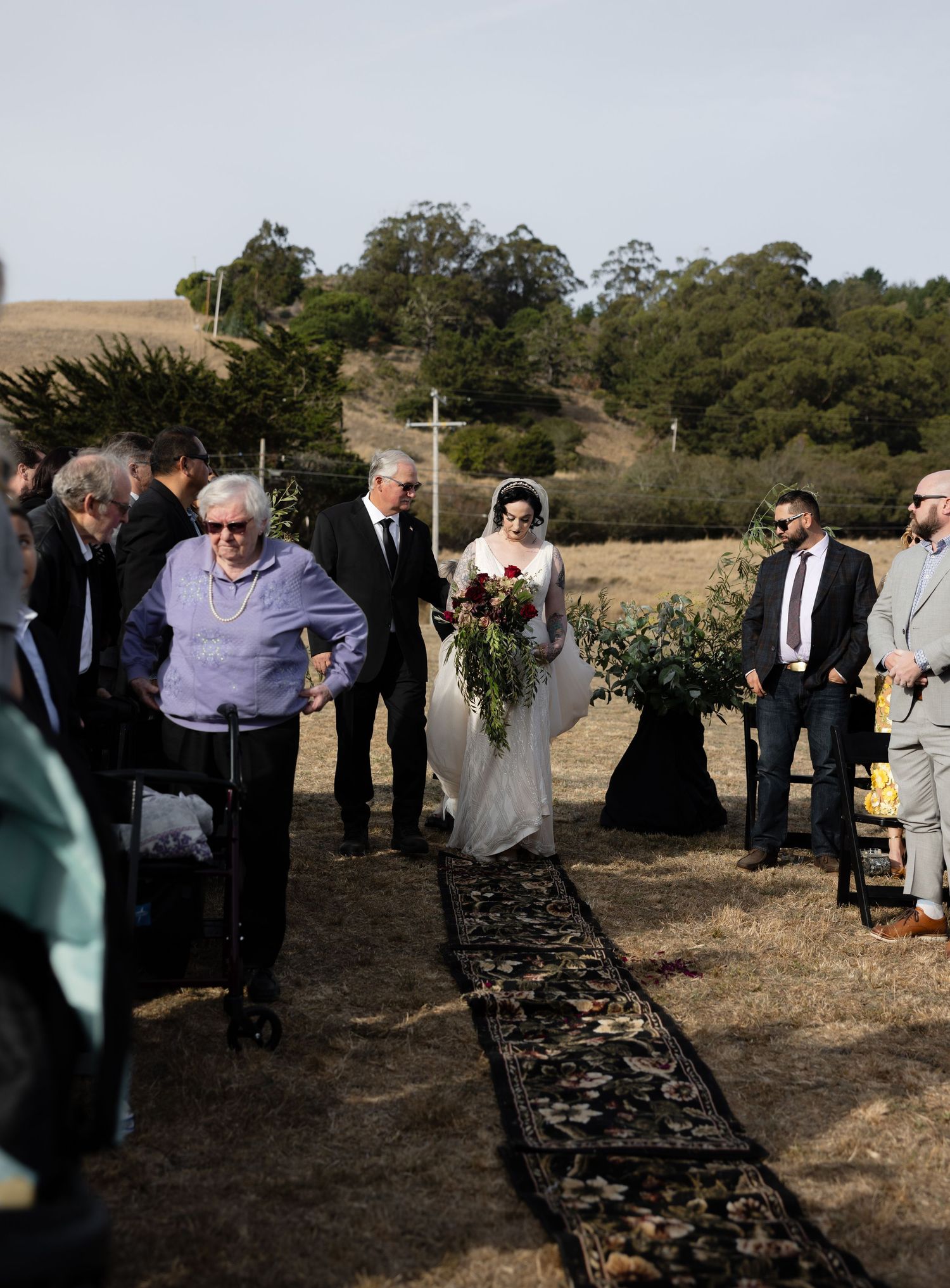 Wedding guests gathering around outdoor seating area with natural landscape backdrop.