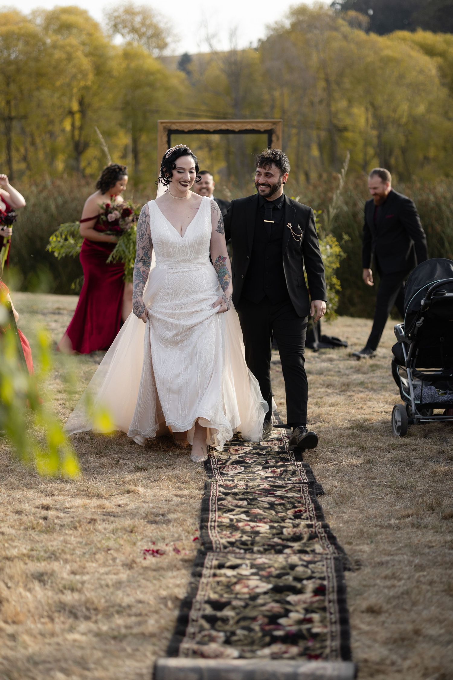 Wedding party walks together along a rustic path through autumn trees and fallen leaves.