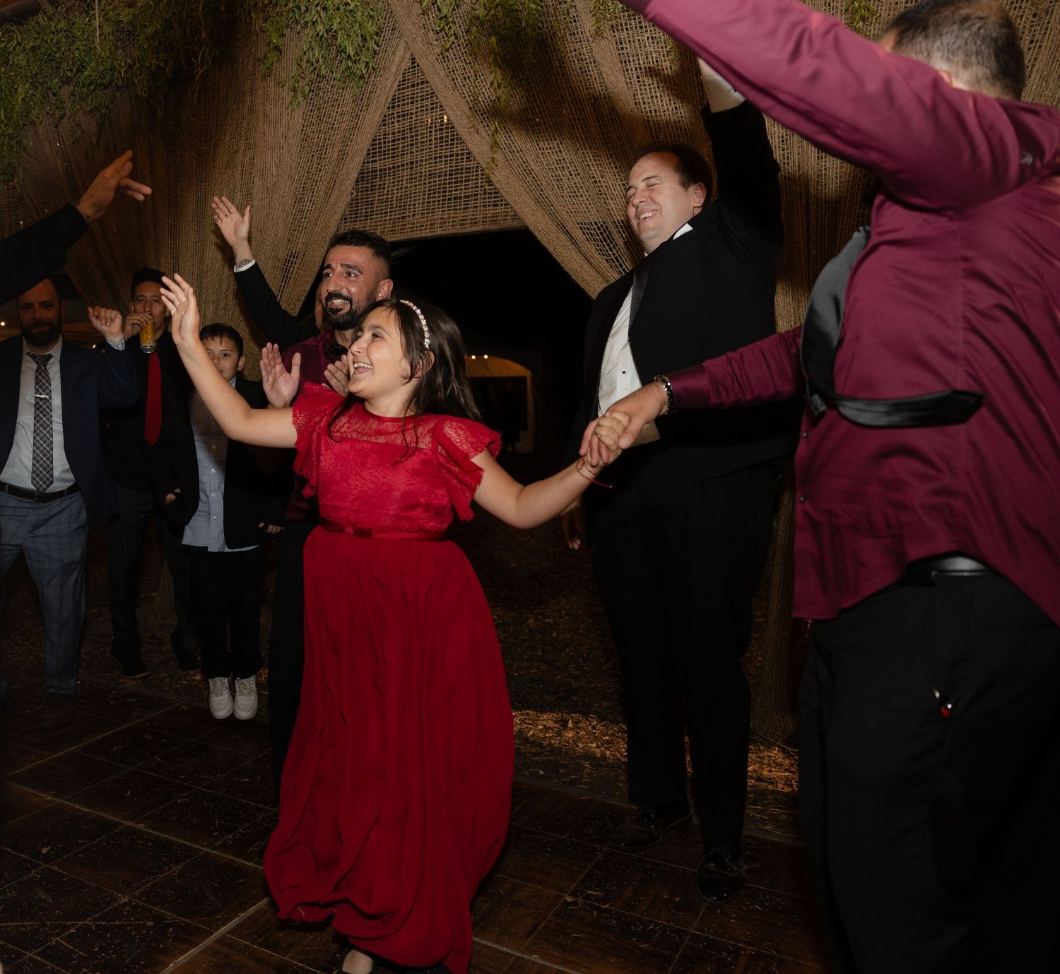 Wedding guests in formal attire dancing enthusiastically with hands raised at reception.