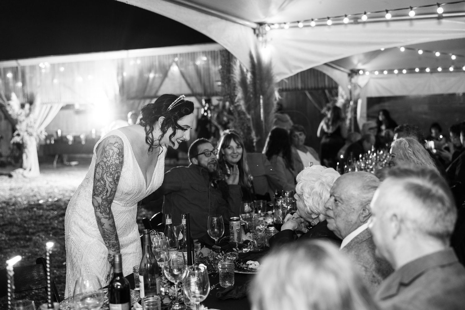 Lively wedding reception scene with string lights and guests mingling at decorated tables.