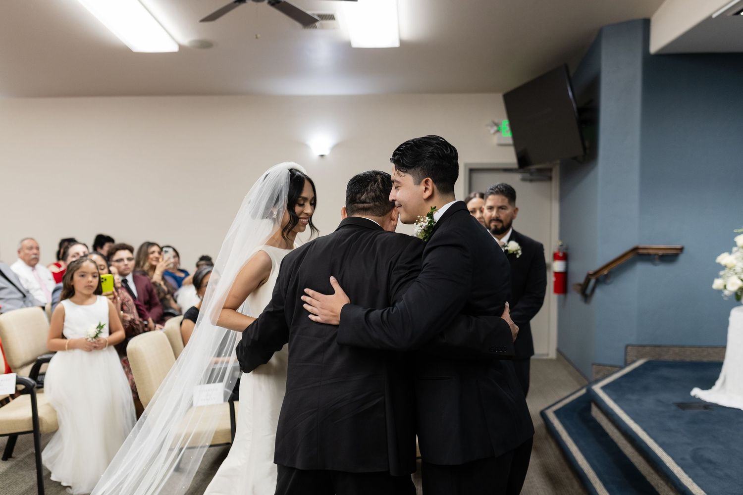Wedding ceremony moment with bride and officiant embracing while guests look on.