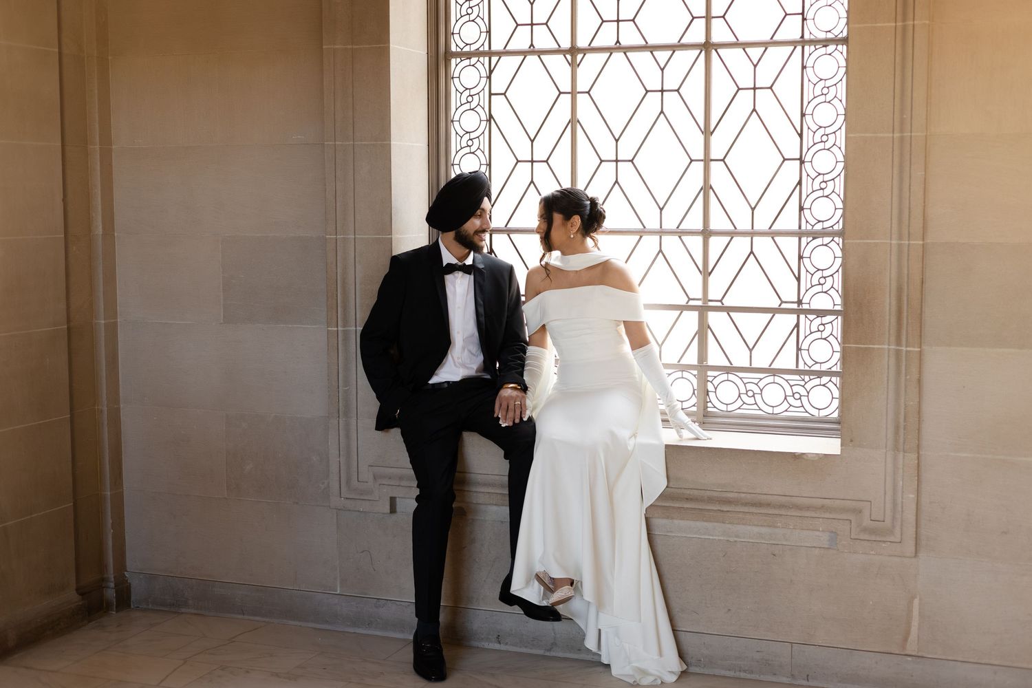 Wedding photography session by large geometric windows in an ornate building.