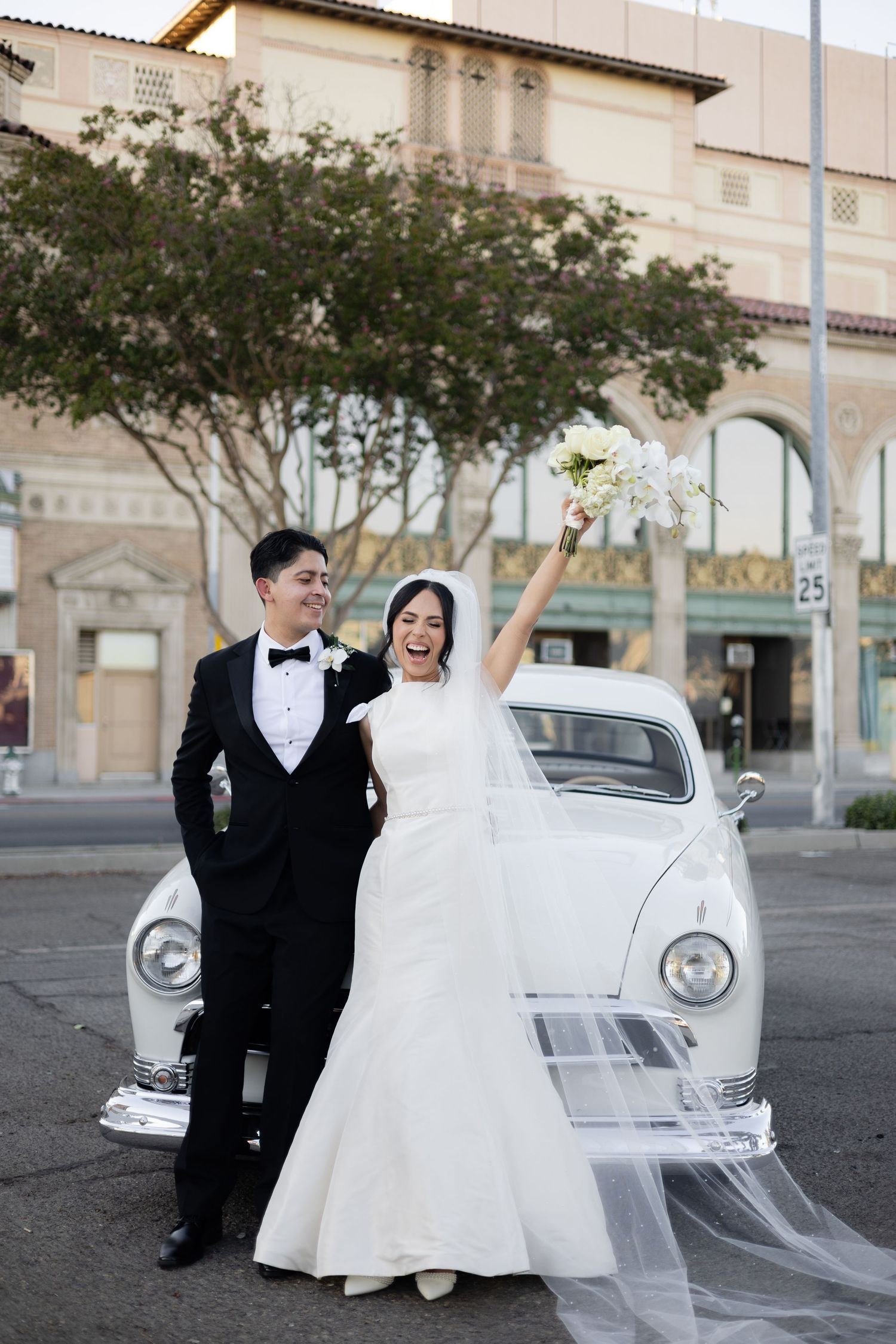 Newlyweds share romantic moment next to vintage white car.