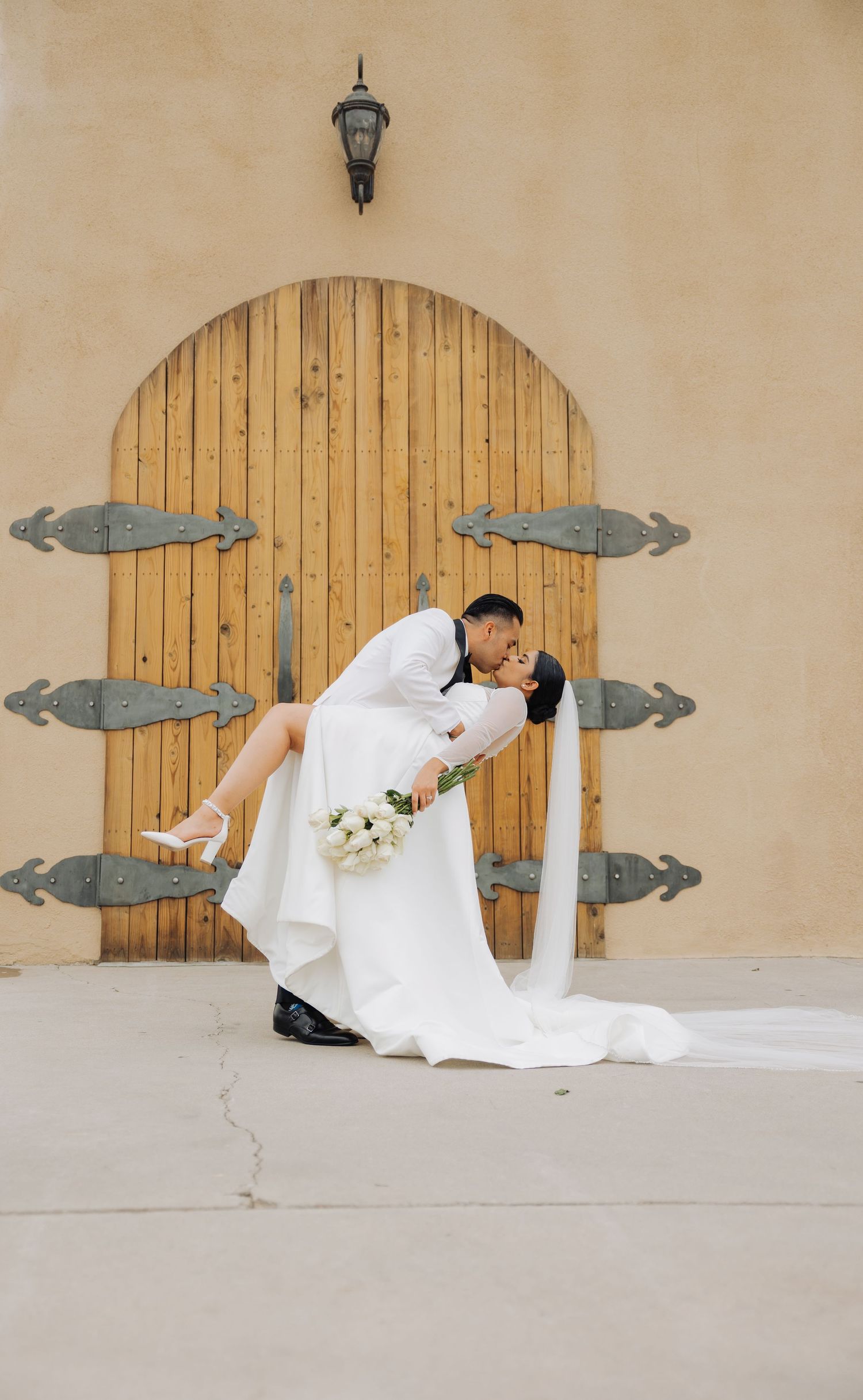 A dramatic dip kiss pose against a wooden door with vintage metal hinges.