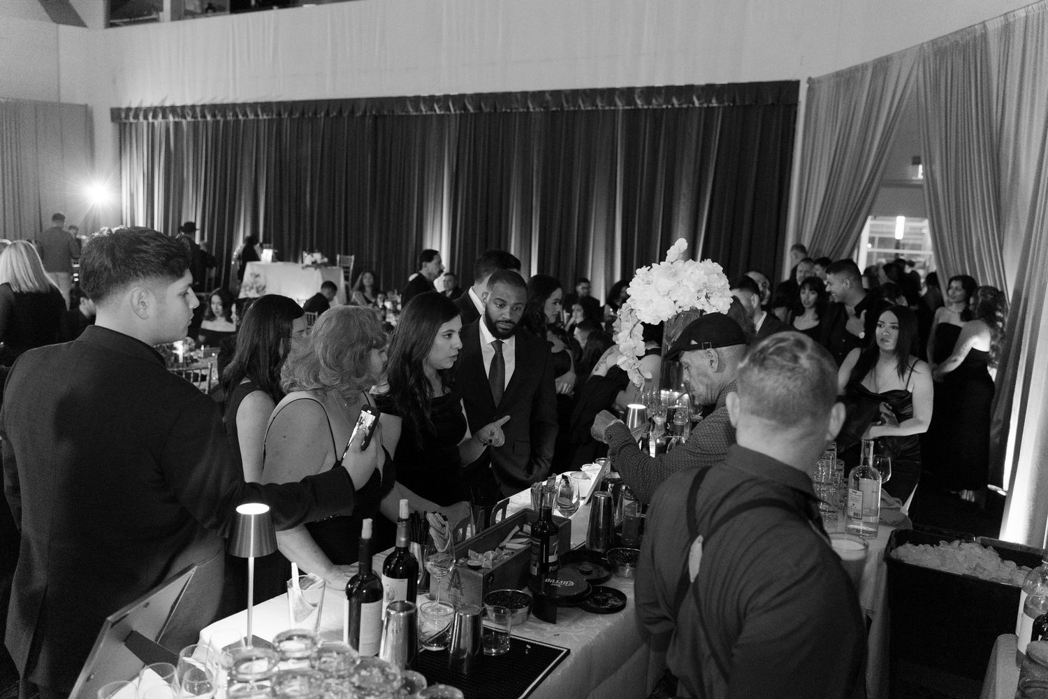 Large group of wedding guests dancing and celebrating in a ballroom with draped walls.