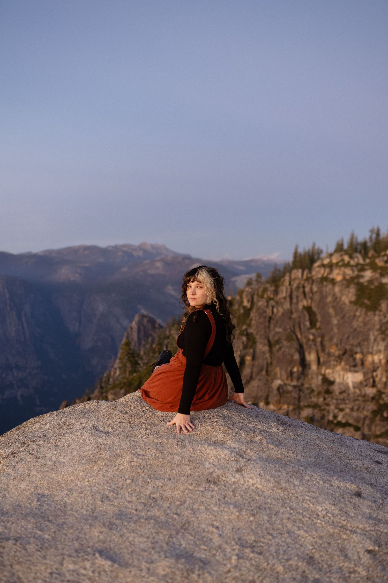 Person in orange clothing lying on granite dome with mountain vista in background.