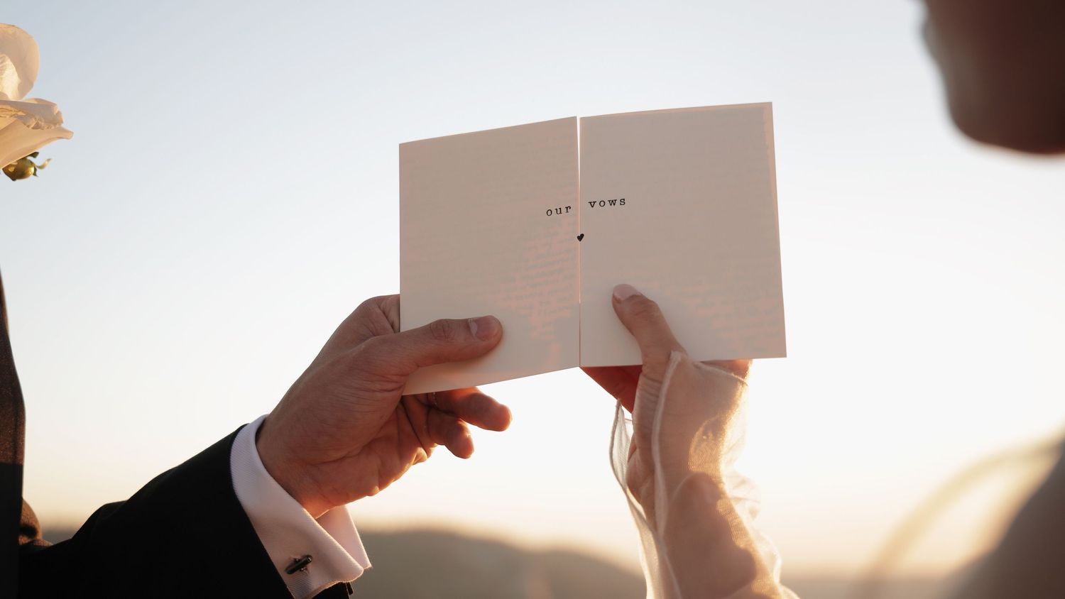 Hands holding wedding vows against sunset sky in Yosemite National Park.