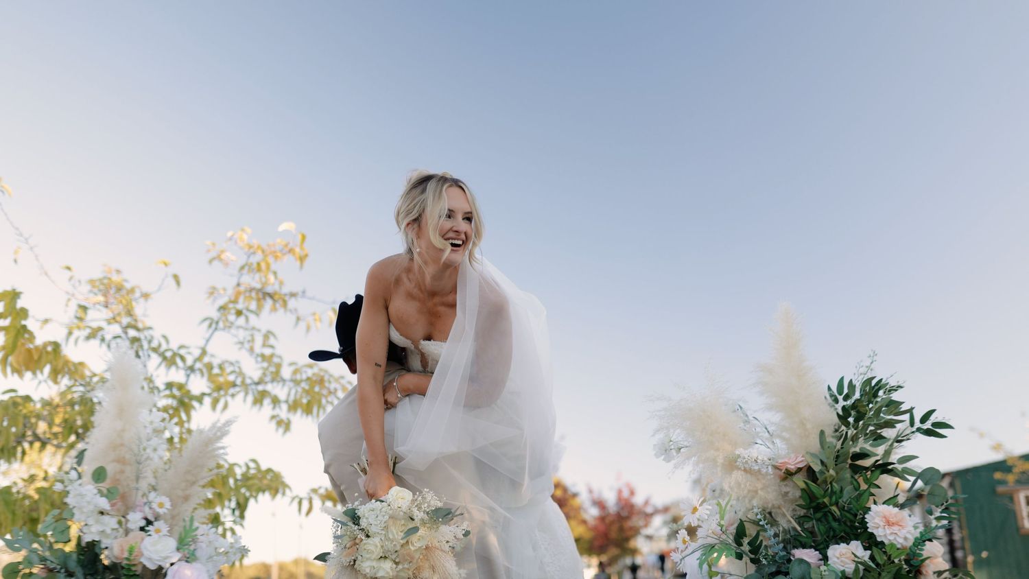 Scenic outdoor wedding ceremony setup with white floral arrangements against a bright blue sky.