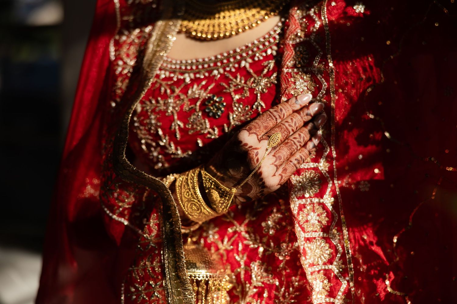 Close-up detail of ornate Indian bridal jewelry and embroidered red wedding dress.