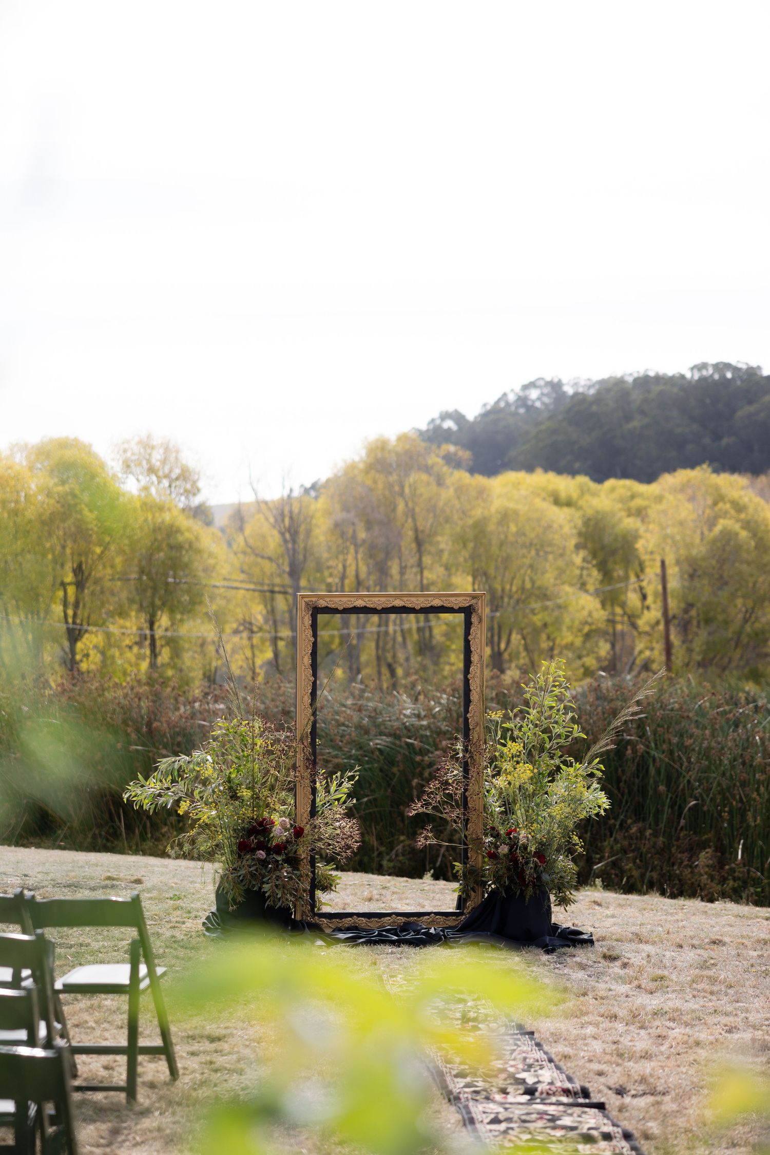 Outdoor wedding arch setup with natural landscape and trees in background.