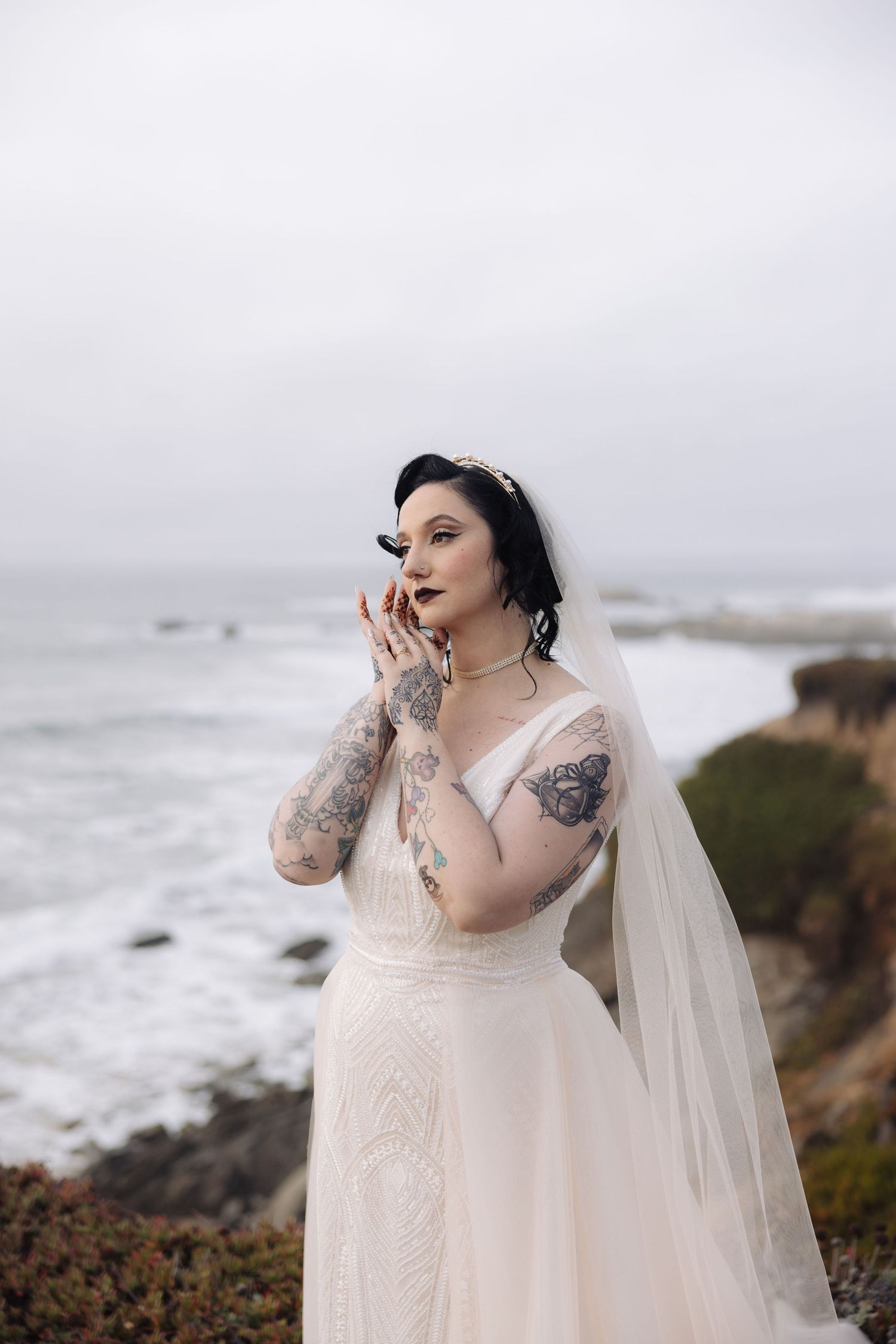 A bride in a flowing white dress poses dramatically on a coastal cliff.
