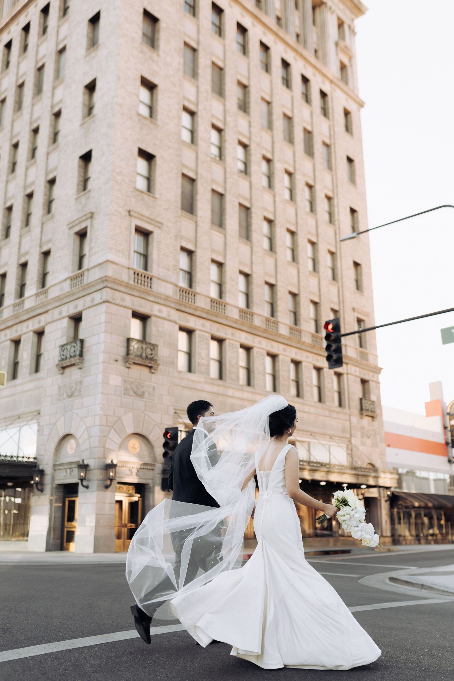 Wedding couple performs romantic dance moves on a city street with dramatic architectural backdrop.